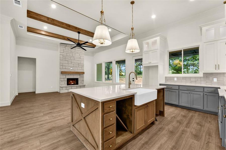 Kitchen featuring ornamental molding, decorative backsplash, gray cabinets, light stone countertops, and an island with sink Kitchen featuring ornamental molding, decorative backsplash, gray cabinets, light stone countertops, and an island with sink