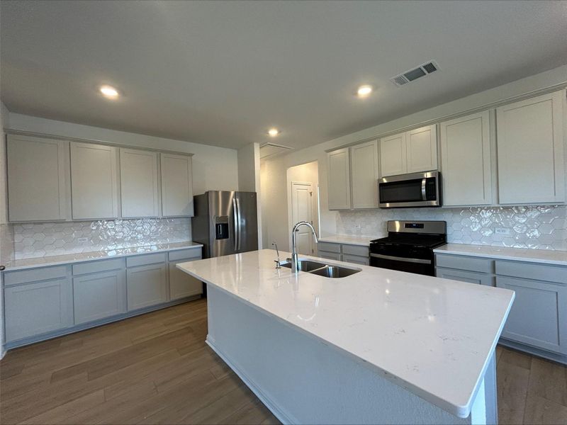 Kitchen featuring decorative backsplash, light stone countertops, appliances with stainless steel finishes, a kitchen island with sink, and recessed lighting