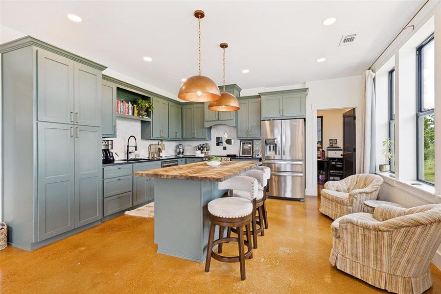 Spacious kitchen featuring custom cabinetry, a large kitchen island with a wood-finish countertop, stainless steel appliances, and polished concrete flooring Spacious kitchen featuring custom cabinetry, a large kitchen island with a wood-finish countertop, stainless steel appliances, and polished concrete flooring