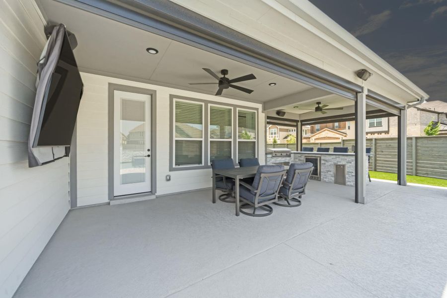 Expansive covered patio featuring two ceiling fans, recessed lighting, and a built-in outdoor kitchen with stone veneer and stainless steel appliances