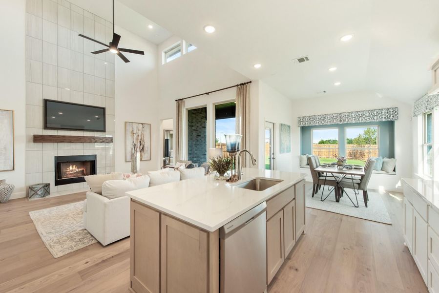 Open-concept living area with kitchen island, fireplace, dining space, and hardwood floors under high ceilings Open-concept living area with kitchen island, fireplace, dining space, and hardwood floors under high ceilings