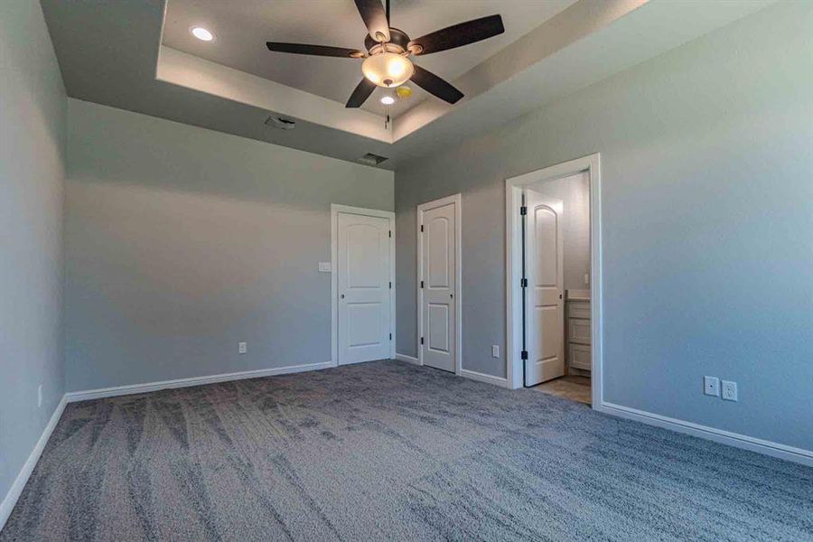 Unfurnished bedroom with a raised ceiling, carpet floors, recessed lighting, a ceiling fan, and connected bathroom Unfurnished bedroom with a raised ceiling, carpet floors, recessed lighting, a ceiling fan, and connected bathroom