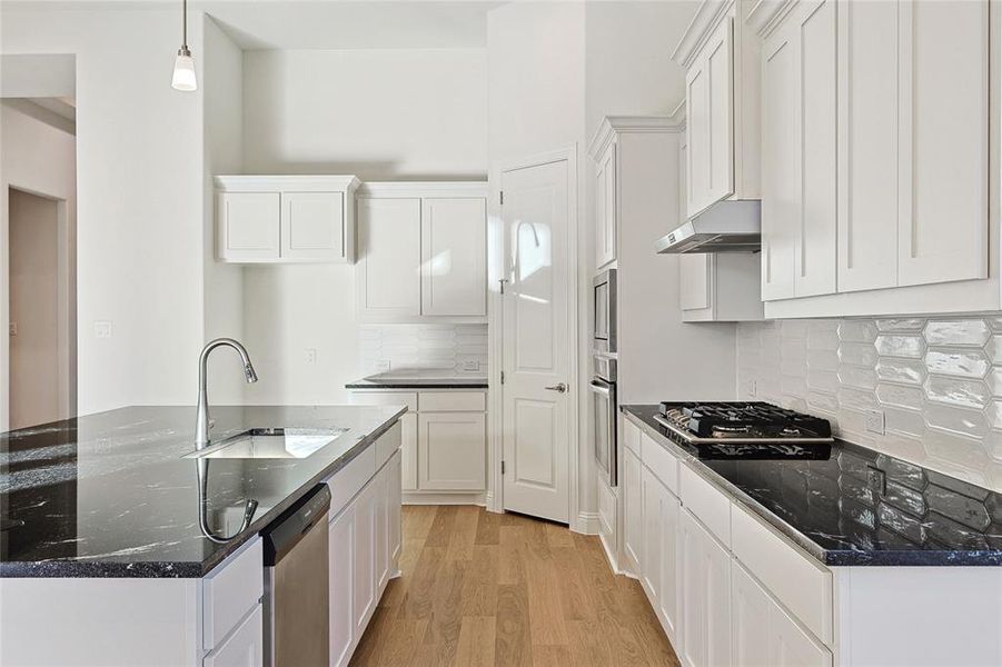 Kitchen featuring light wood-type flooring, decorative light fixtures, appliances with stainless steel finishes, white cabinetry, and sink