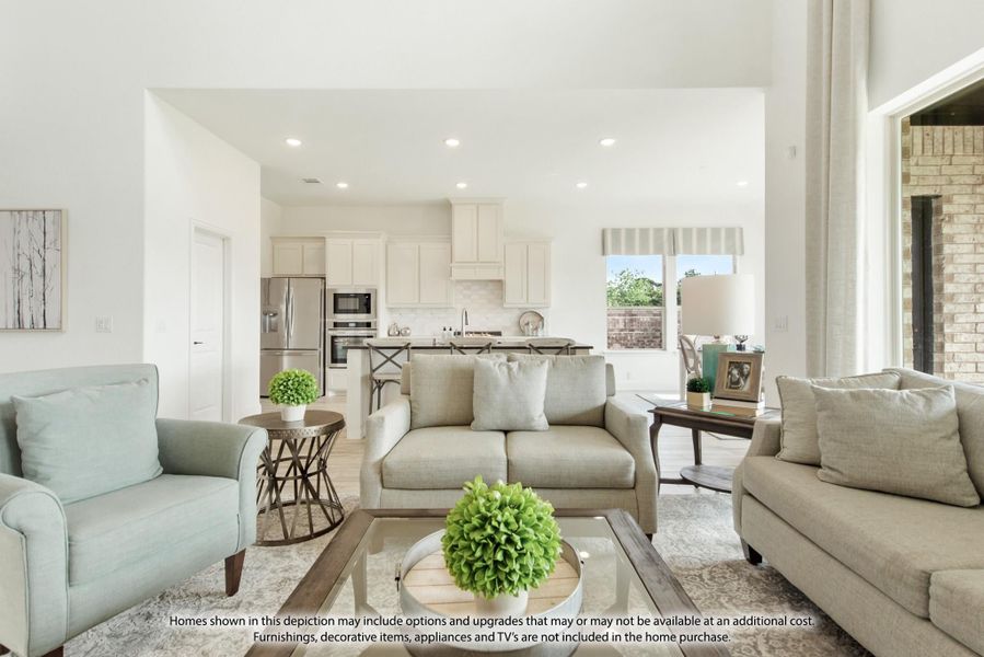 Open-concept living room with gray sofas flowing into a white kitchen with stainless steel appliances and island seating