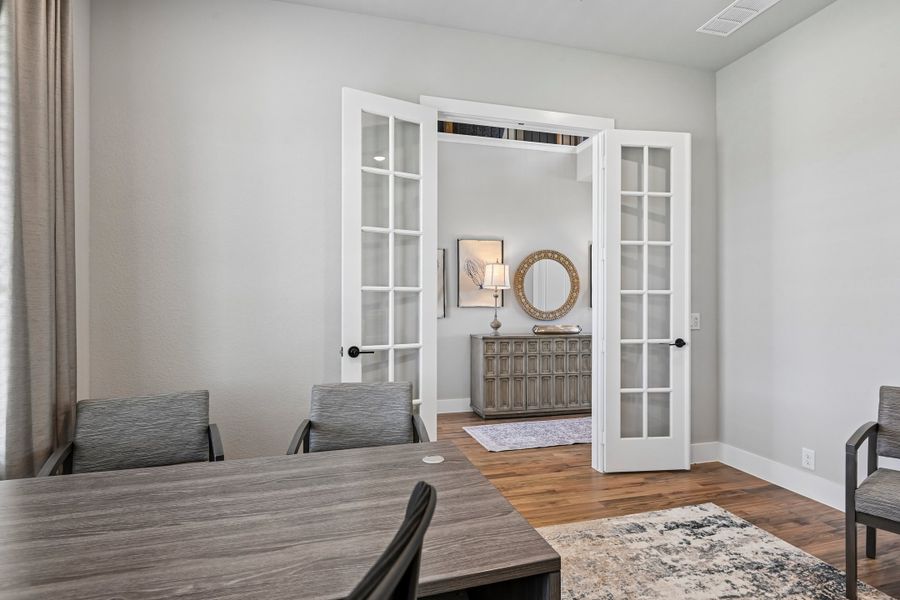 Dining room with wood table, gray chairs, and open French doors leading to a hallway with hardwood floors