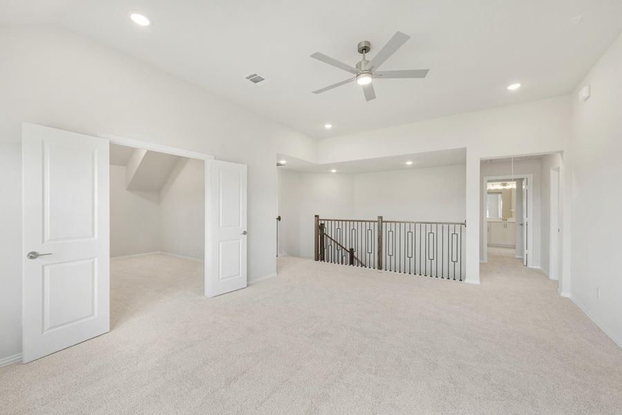 Spacious upstairs loft with carpet, ceiling fan, iron stair railing, and open doors to closet and bathroom