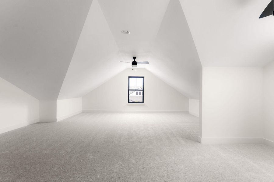 A spacious loft retreat features a peaked ceiling, carpeted flooring, and a window for natural light.