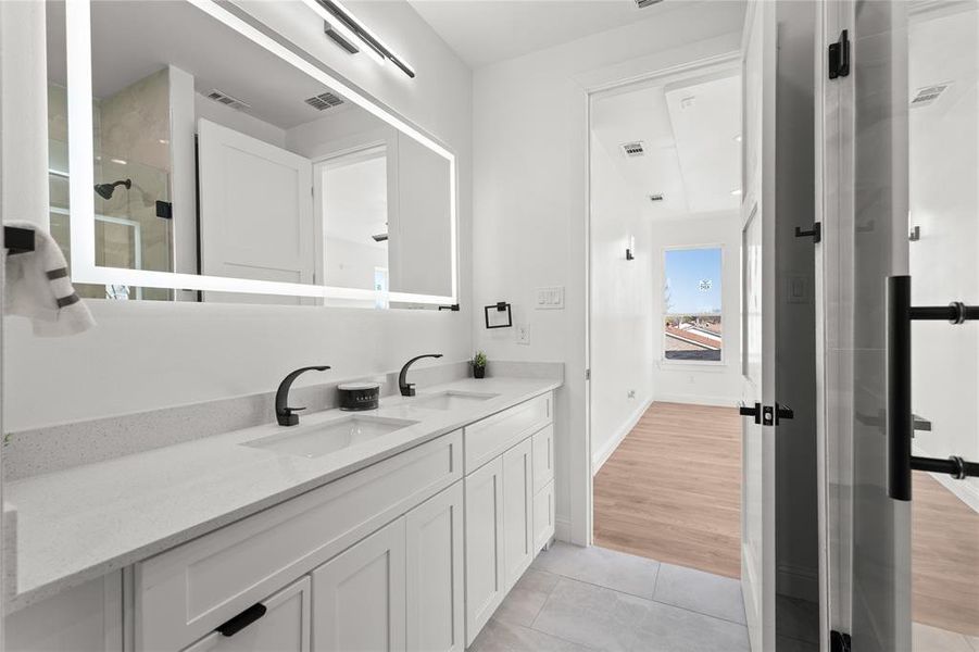 Bathroom with double vanity, light tile patterned floors, and a shower with door