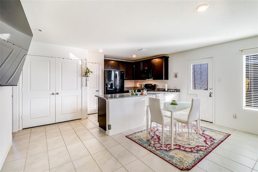 Kitchen featuring dark brown cabinets, black appliances, dark stone countertops, recessed lighting, and light tile patterned flooring