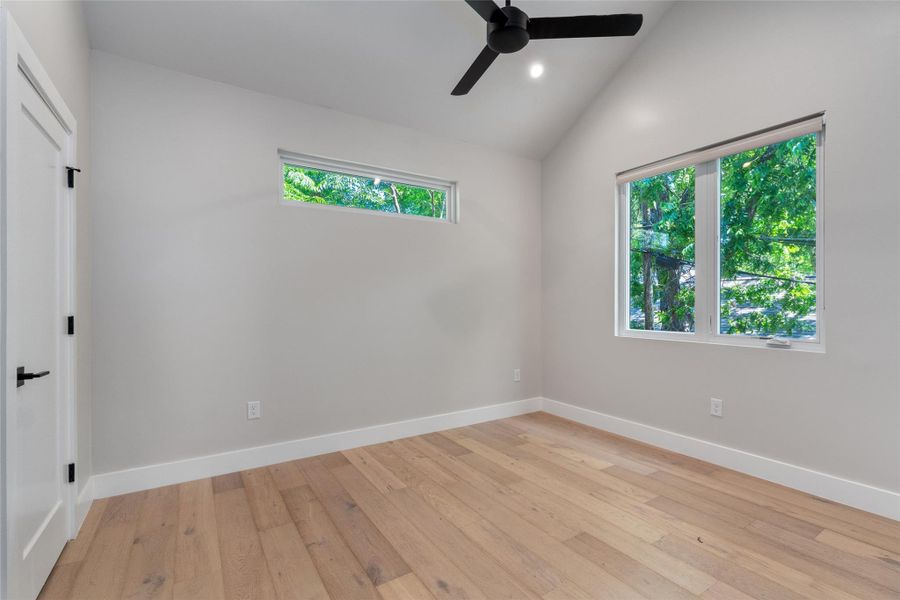 Primary Bedroom featuring vaulted ceilings, wood-finish flooring, and multiple windows. Features a walk-in closet Primary Bedroom featuring vaulted ceilings, wood-finish flooring, and multiple windows. Features a walk-in closet