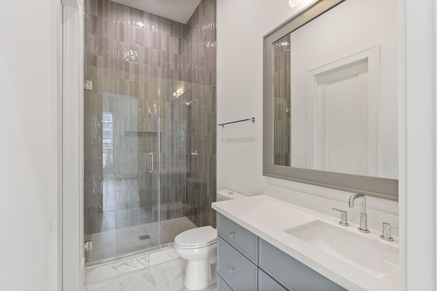 A well-appointed secondary bath features a glass-enclosed walk-in shower with full-height tile, clean lines, and modern fixtures, offering both durability and style.