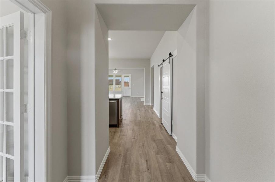 Corridor with a barn door, light wood-style flooring, and recessed lighting