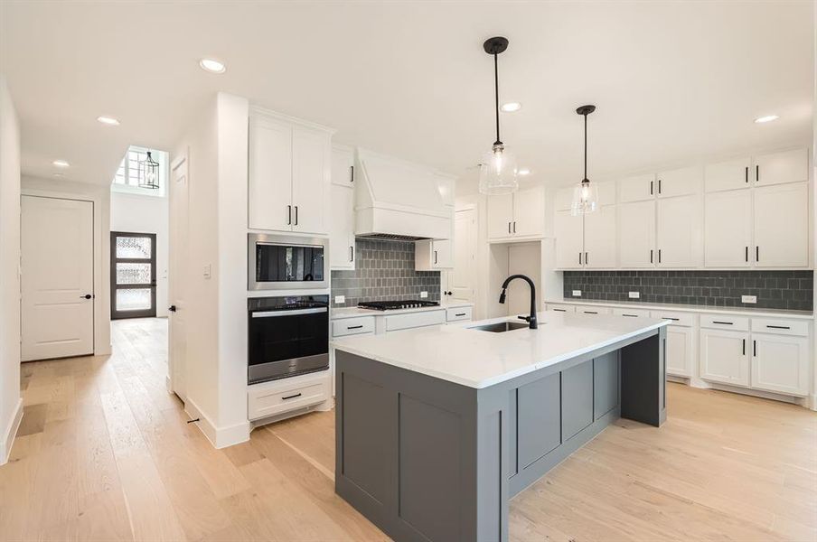 Kitchen featuring a center island with sink, sink, custom exhaust hood, white cabinets, and light wood-type flooring