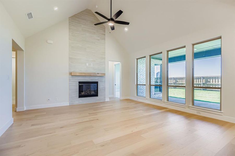 Unfurnished living room featuring high vaulted ceiling, light wood-style floors, a tiled fireplace, and a ceiling fan Unfurnished living room featuring high vaulted ceiling, light wood-style floors, a tiled fireplace, and a ceiling fan