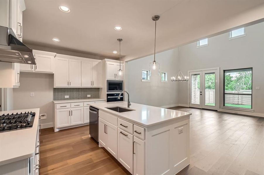 Kitchen with stainless steel appliances, light countertops, wall chimney exhaust hood, white cabinetry, and light wood-type flooring Kitchen with stainless steel appliances, light countertops, wall chimney exhaust hood, white cabinetry, and light wood-type flooring