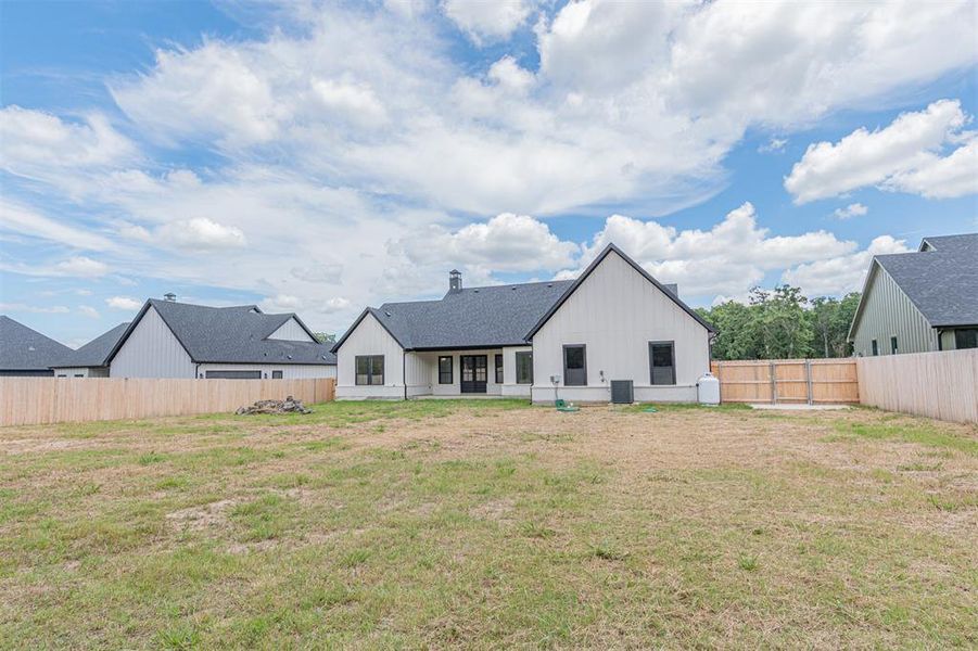 Expansive rear yard featuring a newly constructed residence with white vertical siding and dark trim