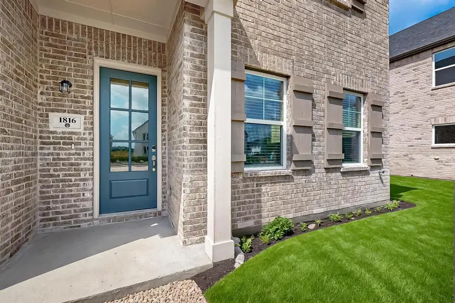 View of exterior entry with brick siding, a porch, and a yard