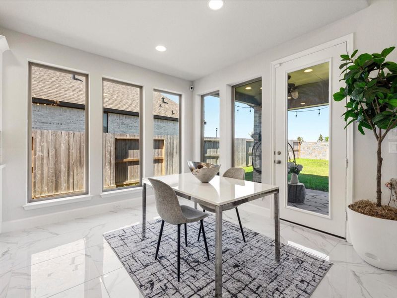 Bright breakfast area with abundant natural light from a wall of tall windows and a glass patio door.