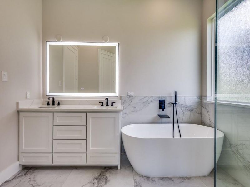 Bathroom featuring marble finish flooring, tile walls, double vanity, a freestanding bath, and a wainscoted wall