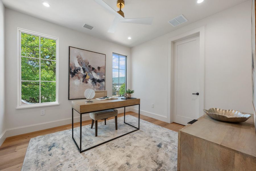 Multi-pane windows illuminate this modern workspace featuring warm hardwood flooring and tall clean-lined doorways.