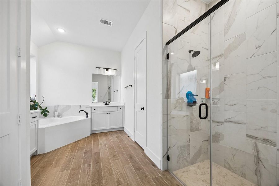 Spa inspired primary bath featuring a frameless glass shower with floor to ceiling tile, matte black fixtures, and a built in bench. Separate soaking tub, dual sink vanity, and wood look tile flooring complete the clean, elevated design. Spa inspired primary bath featuring a frameless glass shower with floor to ceiling tile, matte black fixtures, and a built in bench. Separate soaking tub, dual sink vanity, and wood look tile flooring complete the clean, elevated design.