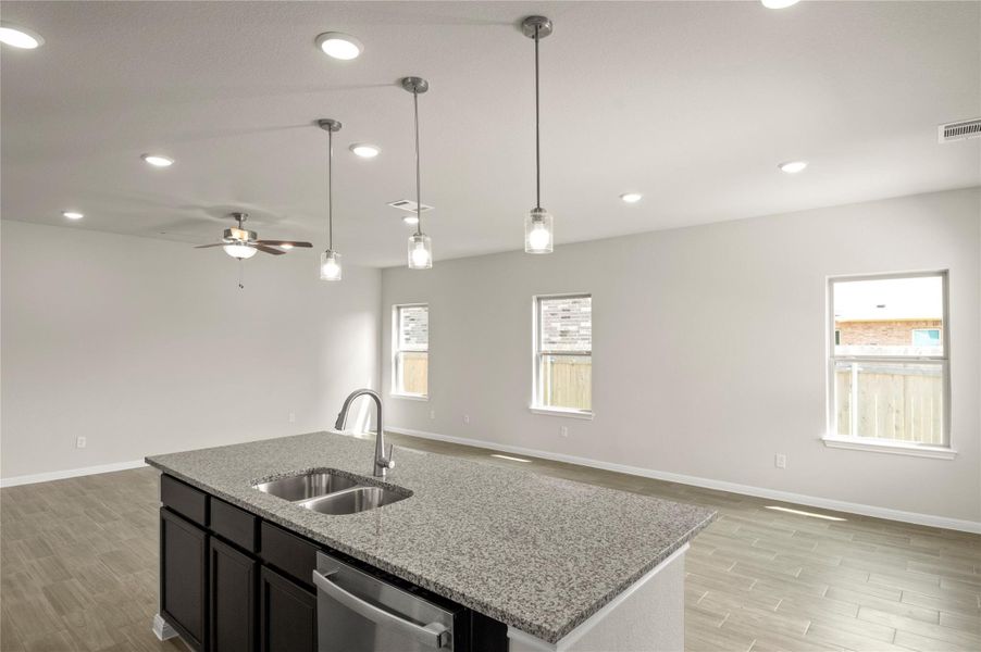 Kitchen with open floor plan, stainless steel dishwasher, light wood-style floors, ceiling fan, and pendant lighting