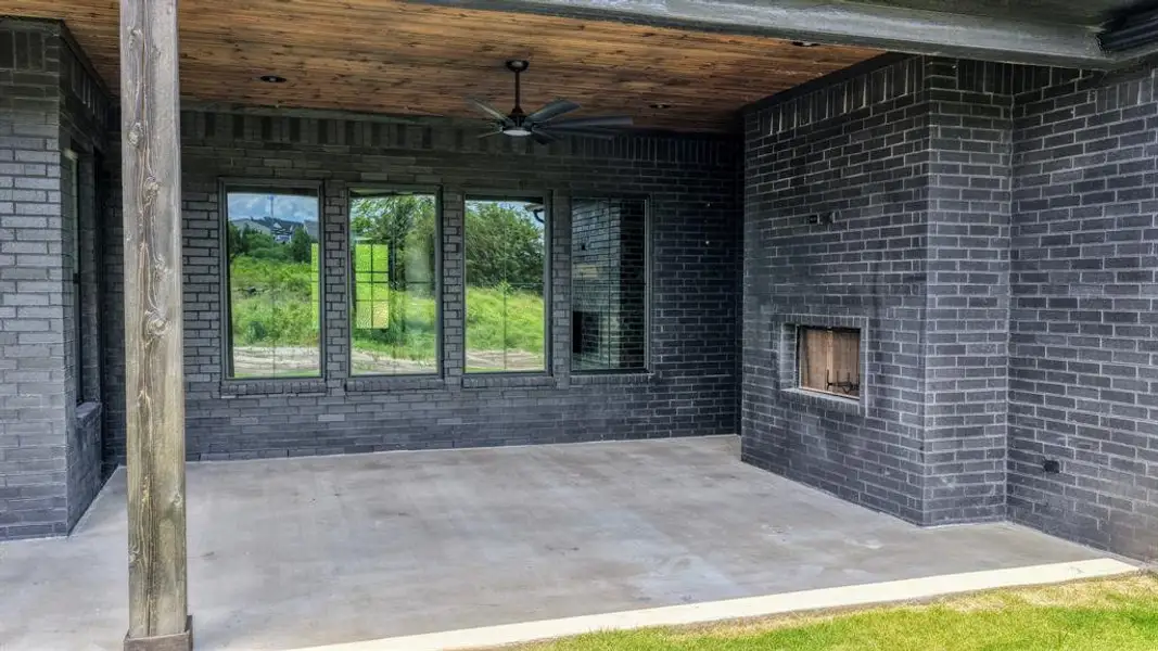 Covered outdoor patio featuring a concrete surface, a built-in outdoor fireplace, and a wood-finish ceiling with an attached ceiling fan