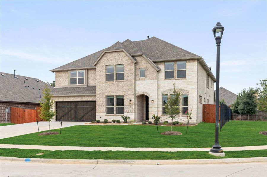 Two-story brick home with three-car garage, arched entry, and manicured front lawn on a corner lot Two-story brick home with three-car garage, arched entry, and manicured front lawn on a corner lot