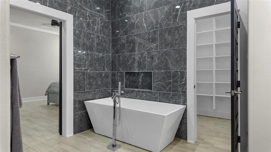 Full bathroom with tile walls, a soaking tub, light wood-style flooring, and ornamental molding