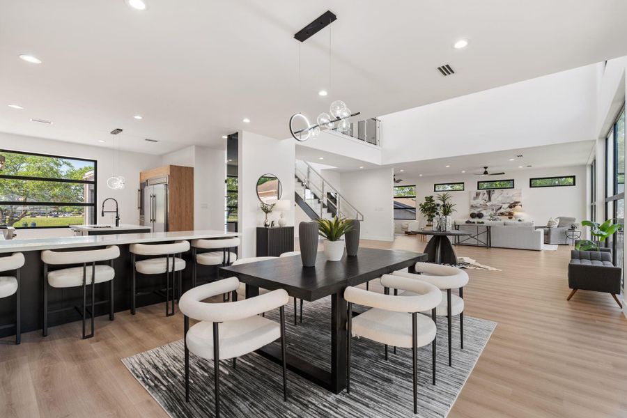 The full open plan reveals itself from here — the dining area in the foreground, the kitchen island and bar seating stretching to the left, the staircase and living room opening beyond tie every element together in this cohesive 1st floor space.
