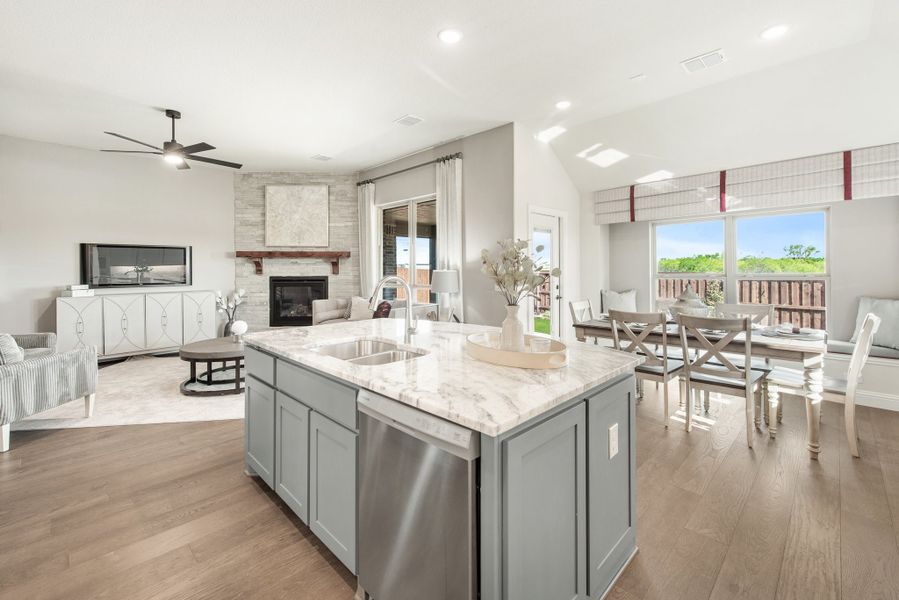Open-concept living area with kitchen island, marble countertops, gray cabinets, and stone fireplace in background