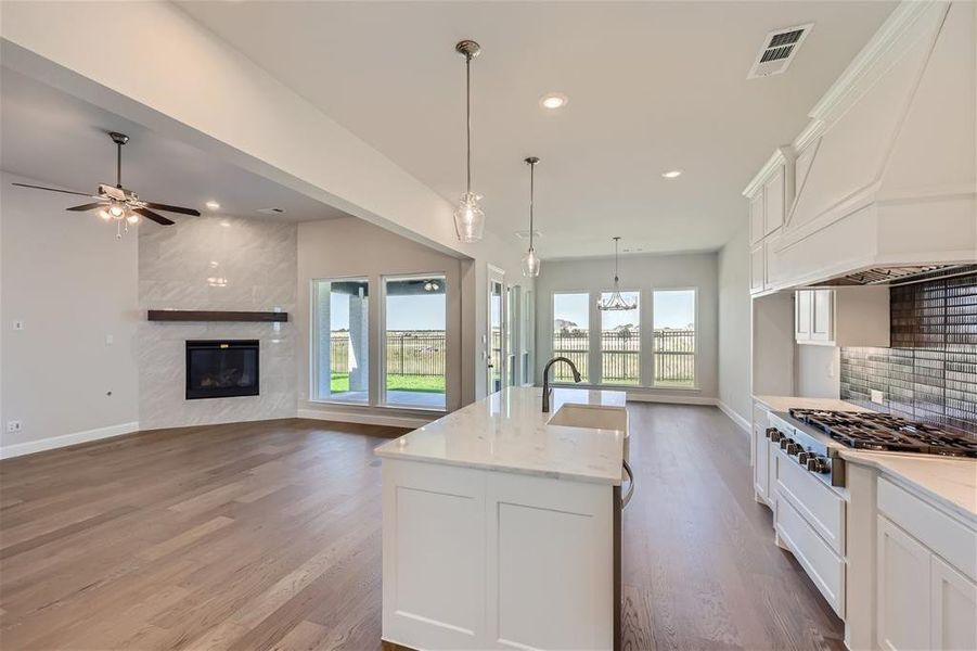 Kitchen featuring a center island with sink, white cabinetry, wood-type flooring, a high end fireplace, and premium range hood