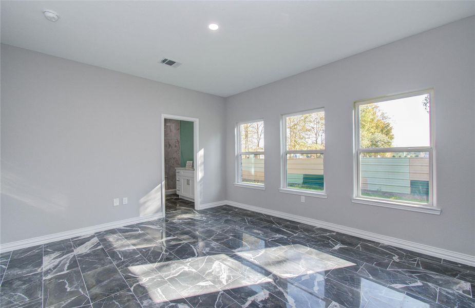 Bright room with glossy black marble flooring, three large windows, and a neutral gray wall color. There's an adjacent bathroom visible through an open door.