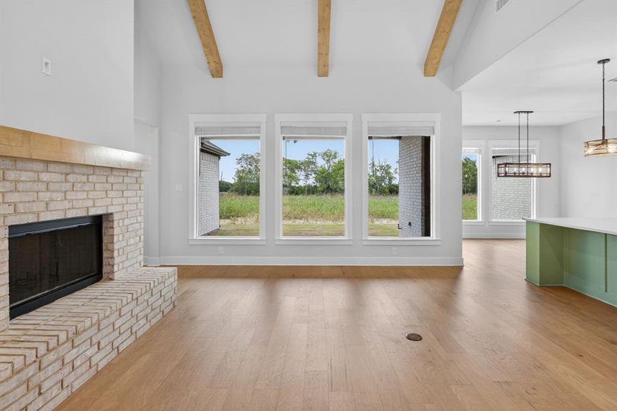 Spacious living area featuring a light-colored brick fireplace with a wood mantel, high vaulted ceilings with exposed wood beams, and light wood-finish flooring Spacious living area featuring a light-colored brick fireplace with a wood mantel, high vaulted ceilings with exposed wood beams, and light wood-finish flooring