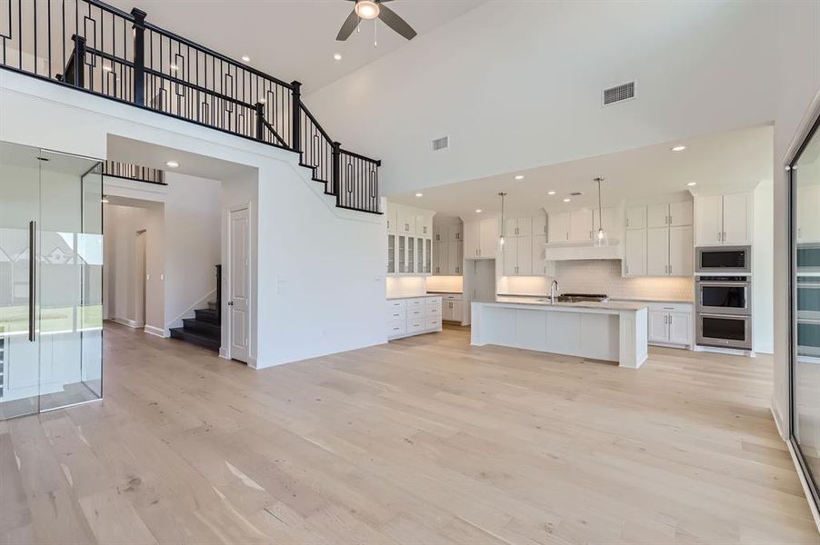 Unfurnished living room with light wood-type flooring, a towering ceiling, ceiling fan, and sink