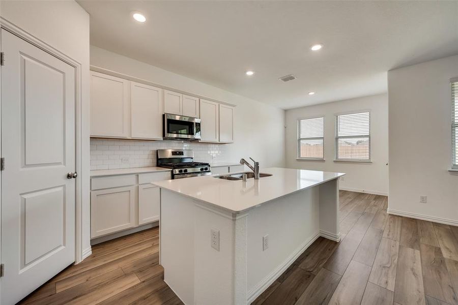 Kitchen featuring hardwood / wood-style floors, stainless steel appliances, a center island with sink, sink, and white cabinetry