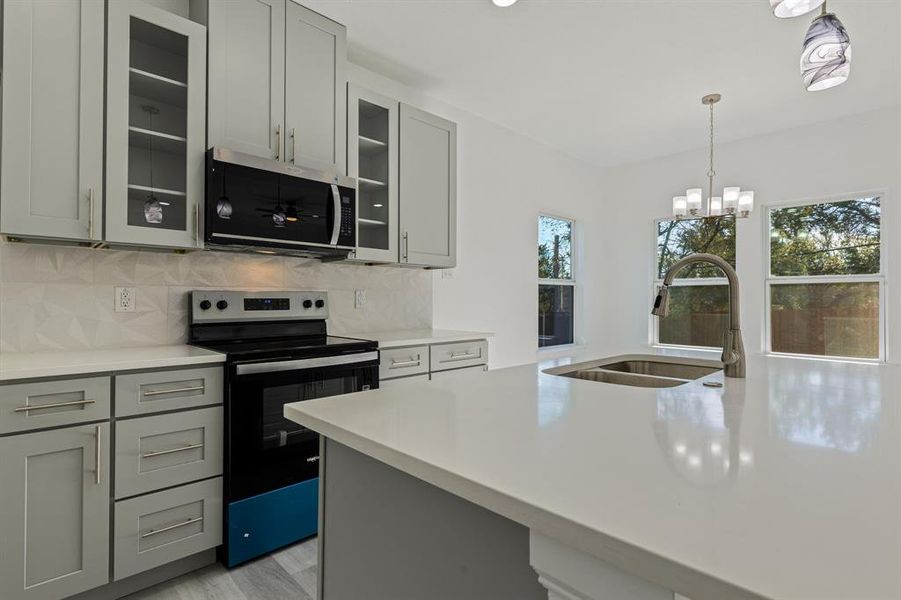 Kitchen featuring appliances with stainless steel finishes, gray cabinetry, glass insert cabinets, hanging light fixtures, and backsplash