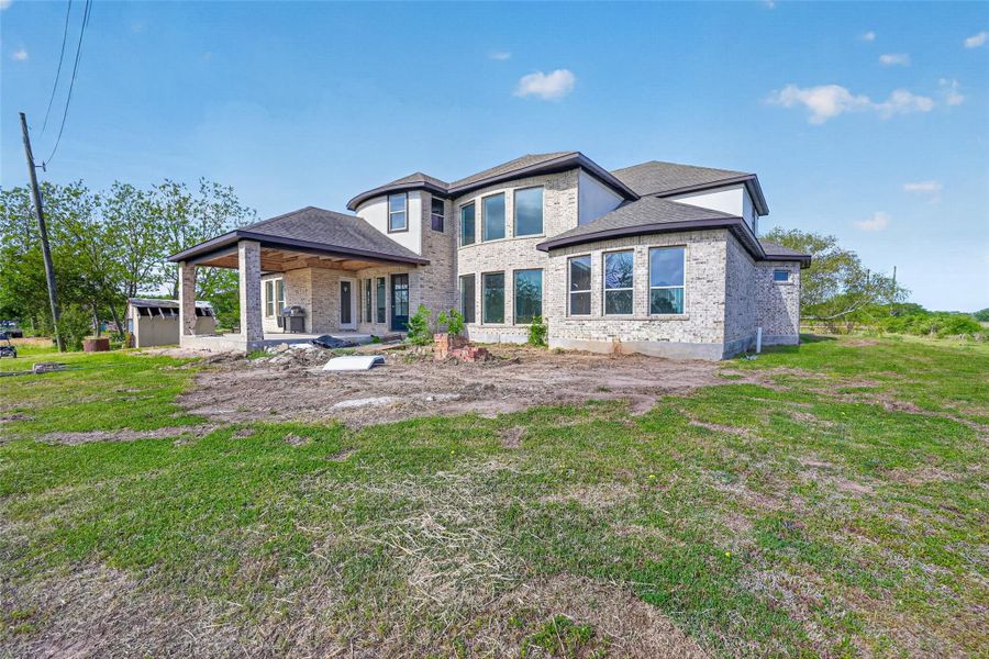 Rear exterior of Property 1 unfinished residence with covered patio, open backyard, and view of the existing lawn.