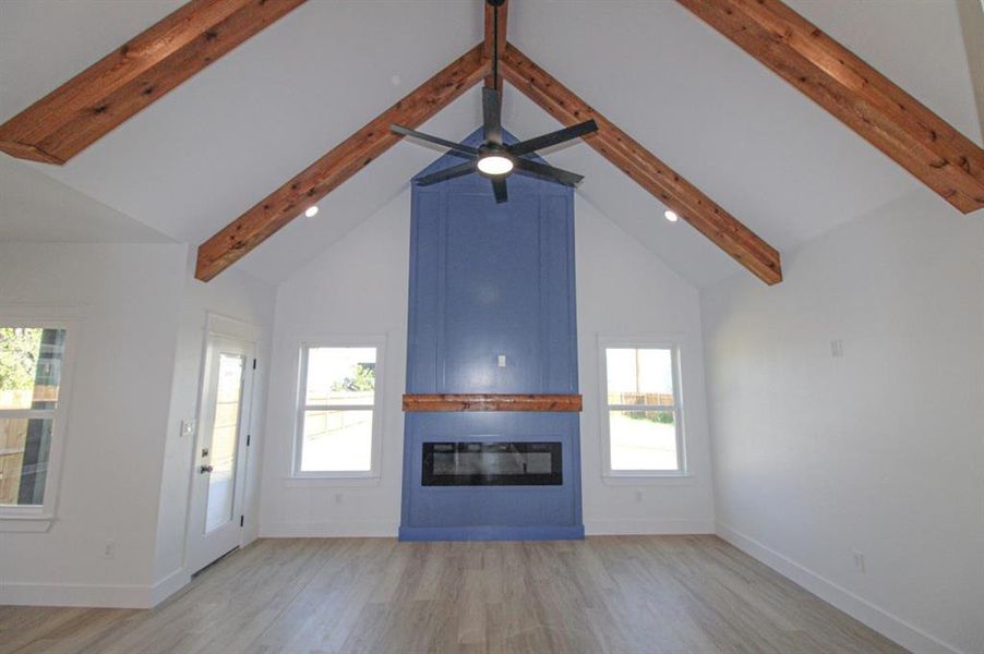 Unfurnished living room with light wood finished floors, a fireplace, beamed ceiling, high vaulted ceiling, and recessed lighting Unfurnished living room with light wood finished floors, a fireplace, beamed ceiling, high vaulted ceiling, and recessed lighting