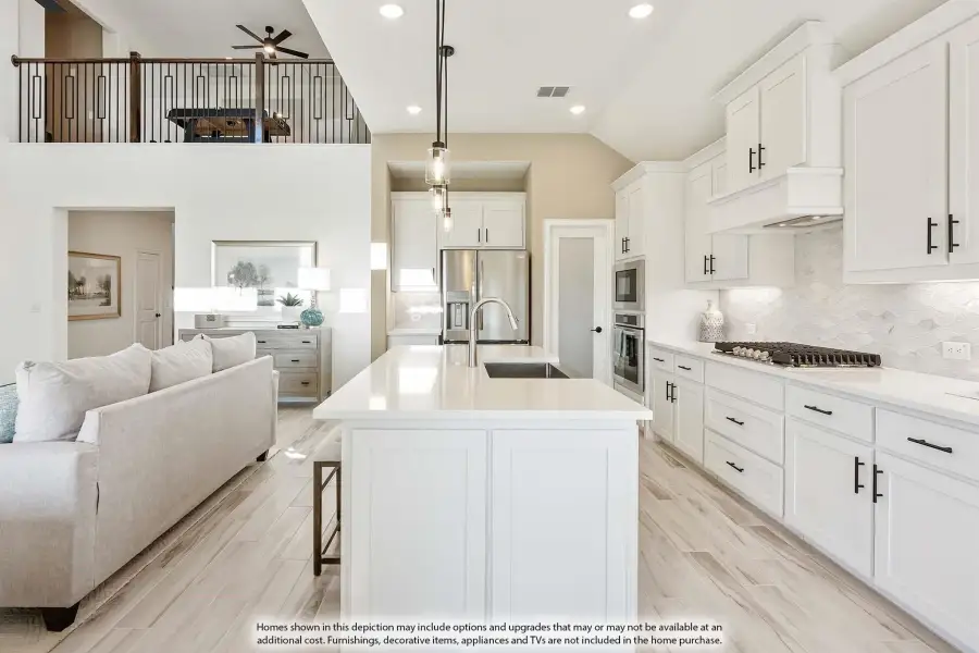 Open-concept kitchen with white cabinets, large island, and stainless appliances, open to living area with second-floor loft above.