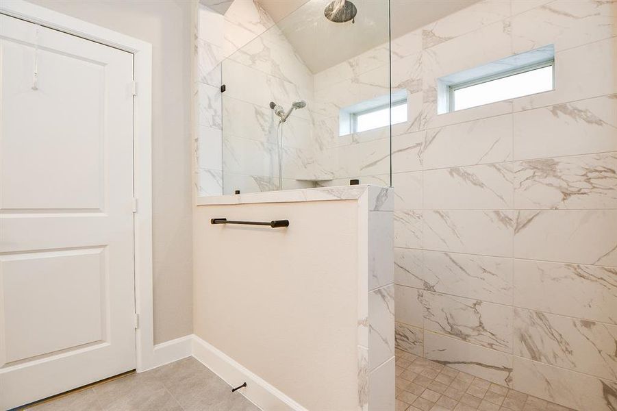 This photo shows a modern bathroom with a spacious walk-in shower featuring elegant marble tiles and dual windows for natural light.