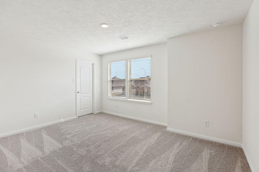 This secondary bedroom offers comfort and style with plush carpeting, neutral paint tones, recessed lighting, large windows with blinds, and a walk-in closet.