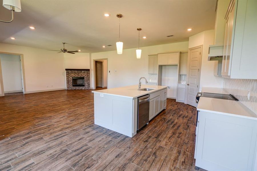 Kitchen featuring recessed lighting, a center island with sink, a fireplace, hanging light fixtures, and light stone countertops Kitchen featuring recessed lighting, a center island with sink, a fireplace, hanging light fixtures, and light stone countertops