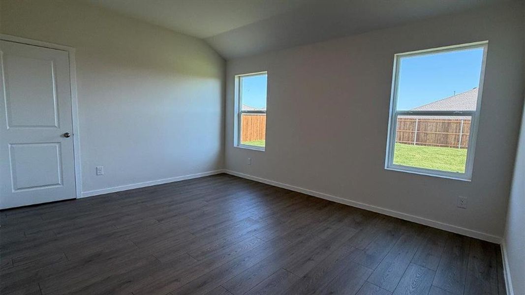 Spacious room featuring wood-finish flooring, two large windows, a single panel door, light-toned walls, and a vaulted ceiling Spacious room featuring wood-finish flooring, two large windows, a single panel door, light-toned walls, and a vaulted ceiling