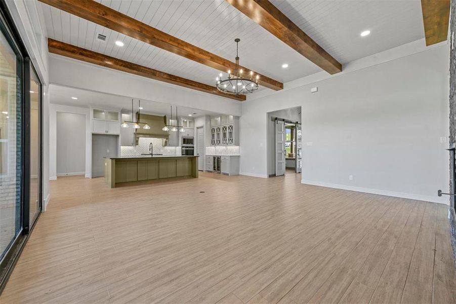 Unfurnished living room with sink, an inviting chandelier, a barn door, light hardwood / wood-style flooring, and beamed ceiling