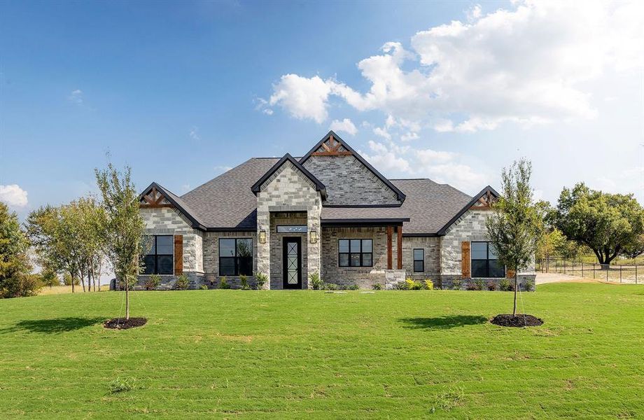 View of front of home with a front yard, stone siding, brick siding, and a shingled roof View of front of home with a front yard, stone siding, brick siding, and a shingled roof