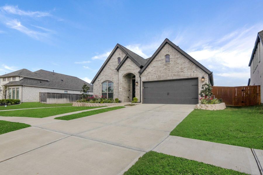 This photo showcases a modern, single-story brick home with a gabled roof and a two-car garage. The front yard features a well-maintained lawn and landscaped flower beds. The driveway is spacious, and the home has a welcoming entrance.