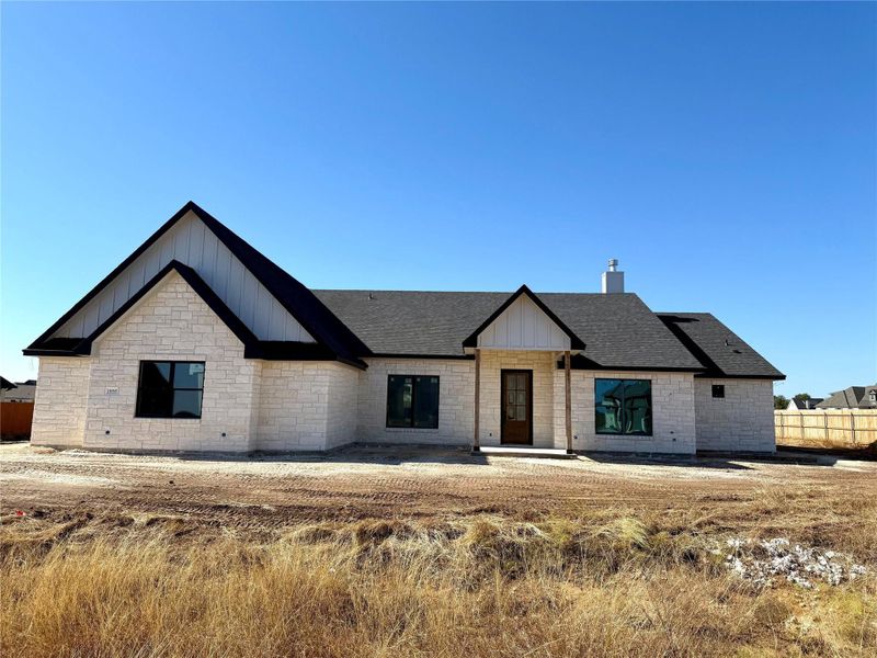 Modern farmhouse featuring board and batten siding, stone siding, covered porch, a shingled roof, and a chimney Modern farmhouse featuring board and batten siding, stone siding, covered porch, a shingled roof, and a chimney