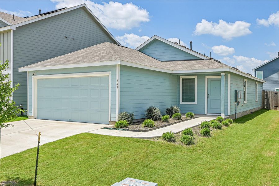 Light blue siding exterior featuring a covered entry, an attached garage, a paved driveway, and manicured landscaping Light blue siding exterior featuring a covered entry, an attached garage, a paved driveway, and manicured landscaping