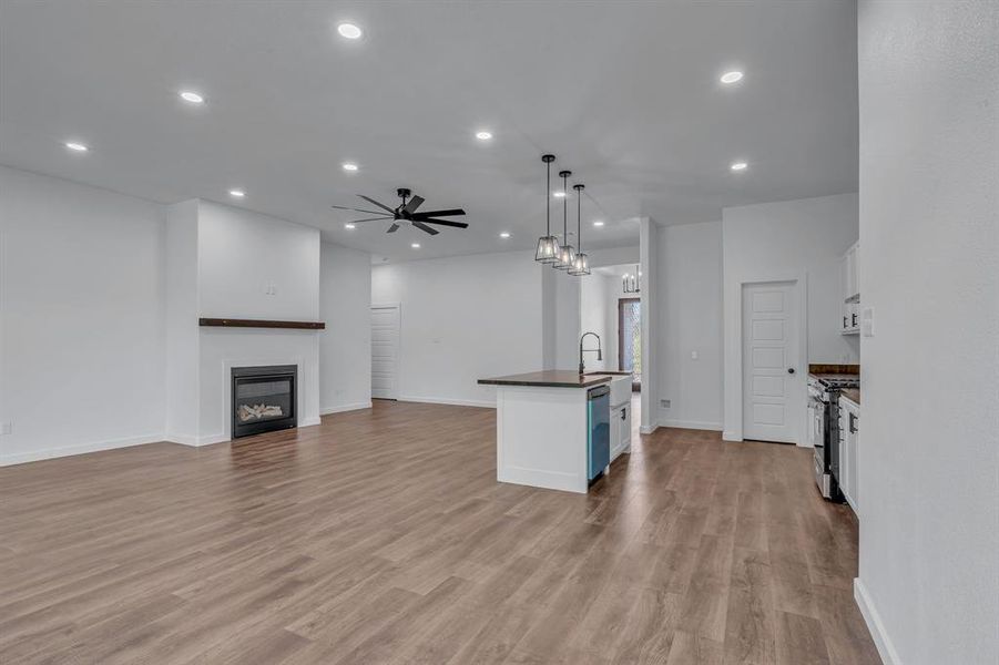 Kitchen featuring white cabinetry, appliances with stainless steel finishes, decorative light fixtures, an island with sink, and light hardwood / wood-style flooring